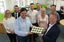 Revilo managing director Lee Collins (left) receives a tray of celebratory cupcakes from Matthew Metcalfe, managing director of Holker IT watched by Revilo and Holker staff and technicians.