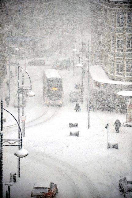 A bus battles through the snow in the city centre.