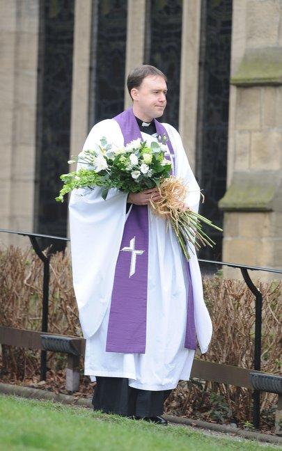 A clergyman carries flowers at the funeral.