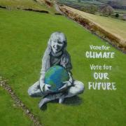 Bradford-born artist Jamie Wardley has created a 165ft (50m) high anamorphic painting of a girl holding the Earth in a Hebden Bridge field to mark Earth Day.