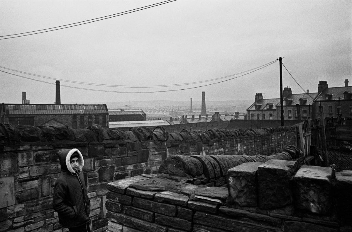 A young boy in an alleyway on his estate, with the industrial sprawl of the city in the background