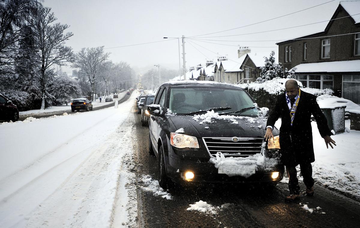 A man clears snow from the front of his car as he waits in the queue