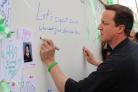 David Cameron pens a message of support on a wall set up by parents campaigning for a Birkenshaw high school