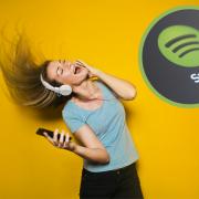 A woman singing to your music listening to headphones. ( Canva) Spotify logo. (PA)