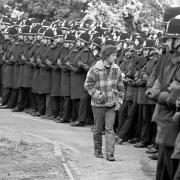 A picket calmly ‘inspects’ a line of linked policemen outside the Orgreave coking plant near Rotherham (PA)